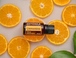 Clementine essential oil bottle with fresh orange slices and green leaves in a round dish.